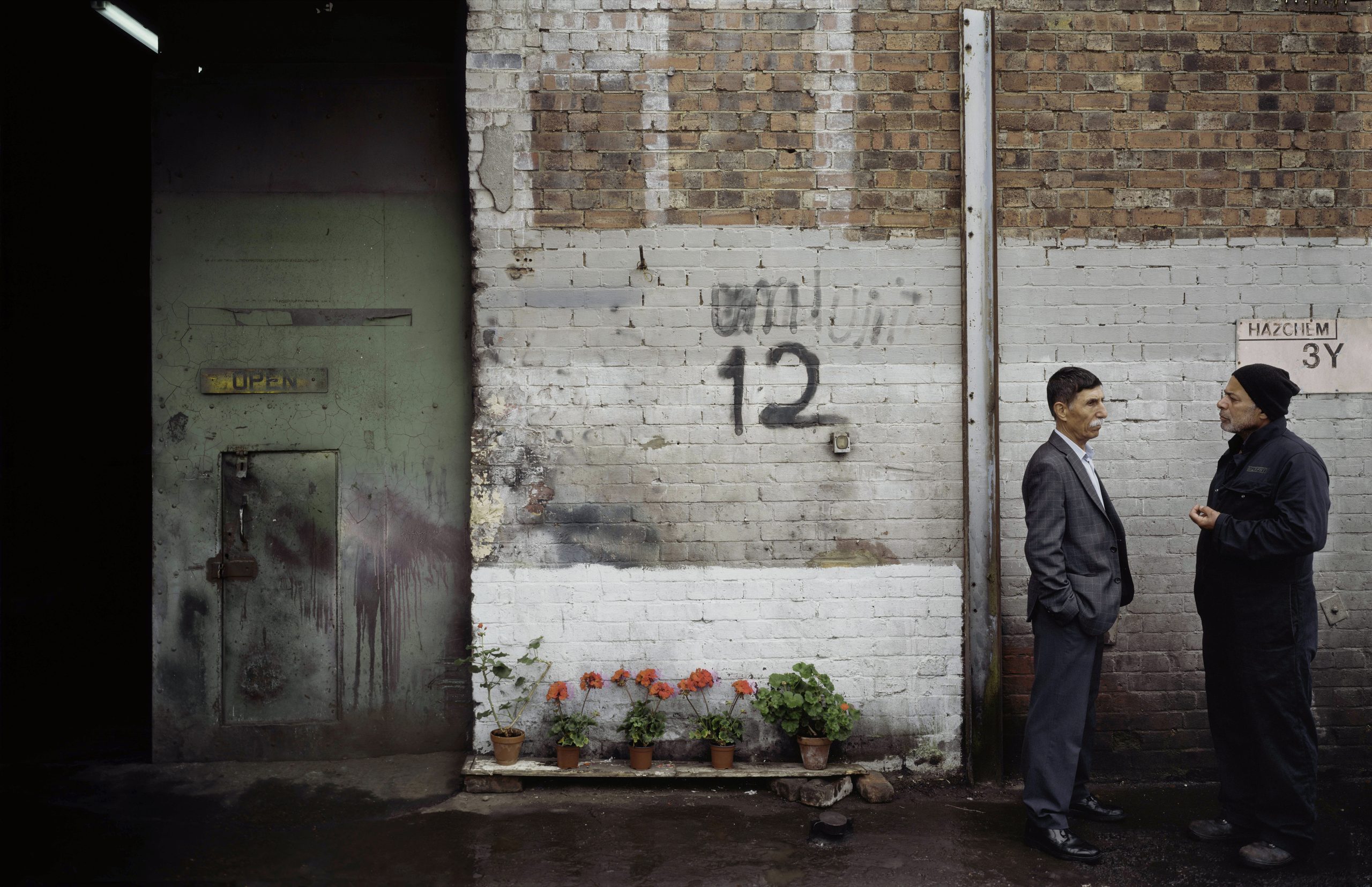 Photograph by artist, Mitra Tabrizian. In a backstreet, two men are facing each other and having a conversation.