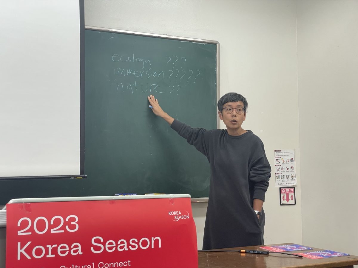 Photograph Prof. May Adadol Ingawanij giving feedback to students at Sogang University. Ingawanij is standing next to a blackboard, pointing at the words 'ecology???' 'immersion????' 'nature???'