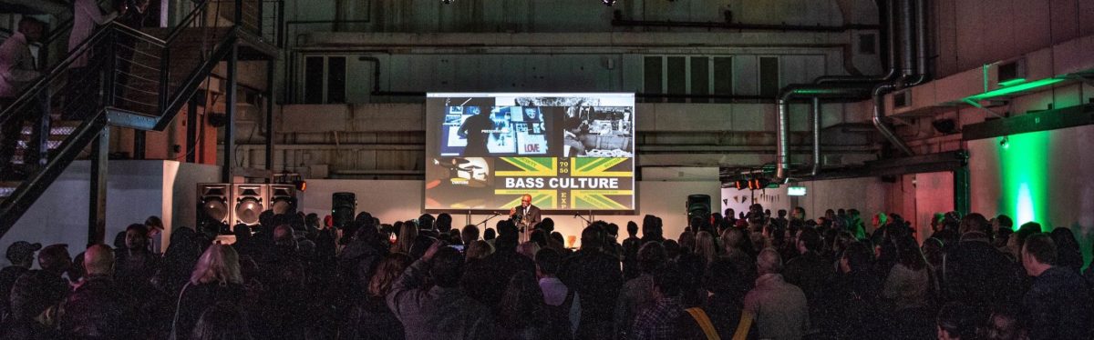 Crowd and speaker on stage at Bass Culture exhibition event at Ambika P3