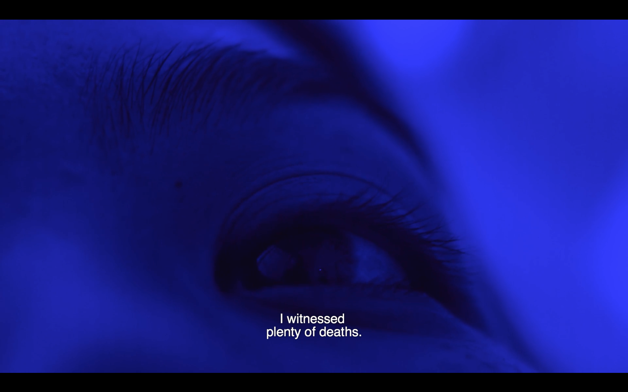 Filmstill by artist Thuy-Han Nguyen-Chi, from the film 'The In/Extinguishable Fire'. Close up of an eye, all in blue with the caption 'I witnessed plenty of deaths'.
